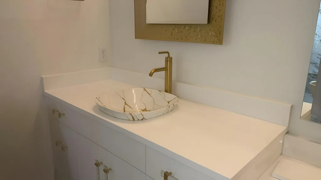 Vanity with a vessel sink and a gold faucet on a light stone top