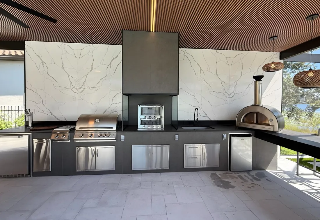 Outdoor kitchen with a full stone backsplash panel, built in grill and pizza oven