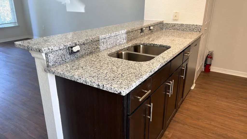 Speckled granite kitchen countertop with an undermount double sink and dark cabinets