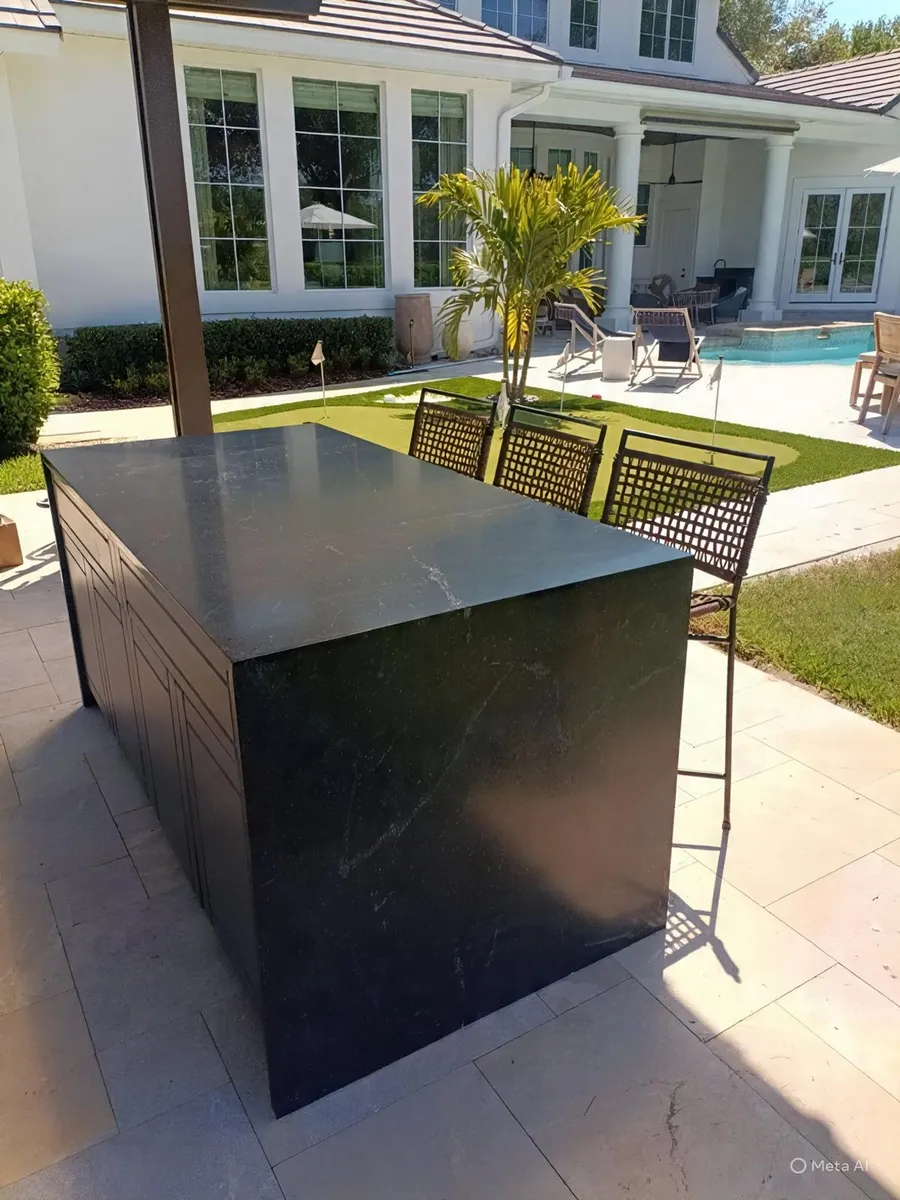 Freestanding outdoor island in a dark stone next to a pool