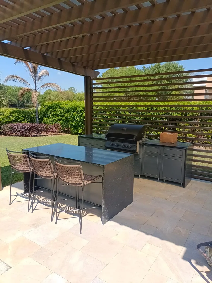 Outdoor kitchen under a pergola with a dark stone bar top and a built in grill
